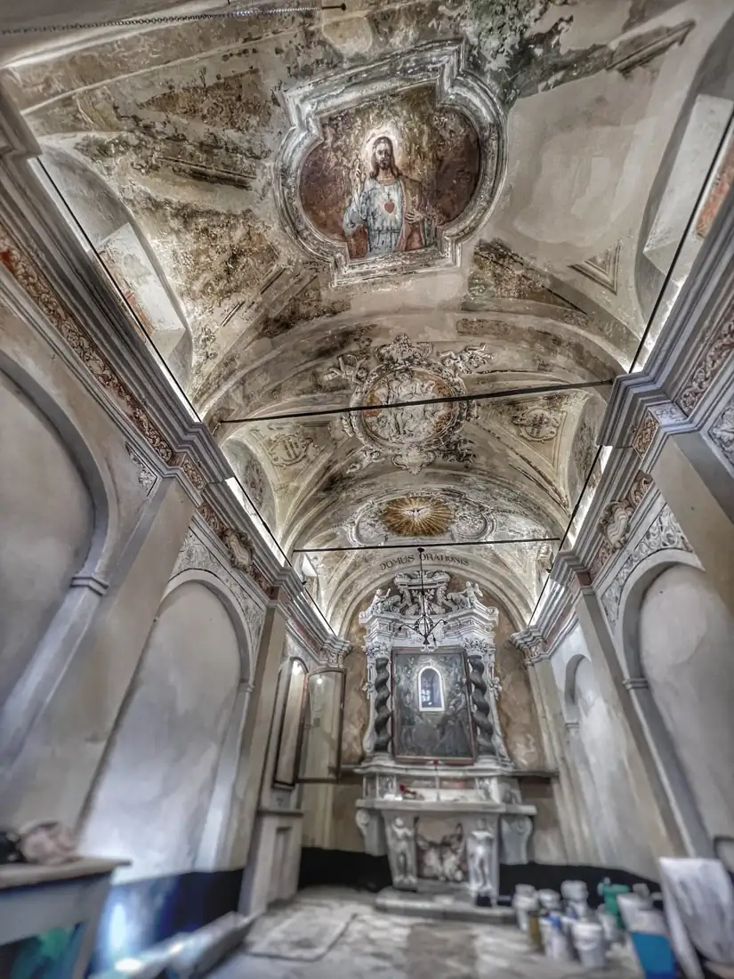 Interno dell'oratorio durante il restauro: volta affrescata con il Sacro Cuore e la colomba dello Spirito Santo, stucchi e altare barocco in fondo, latte di materiale sul pavimento