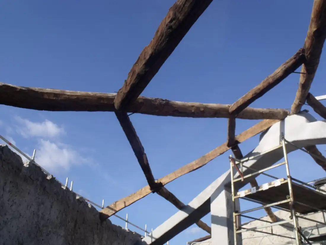 Durante i lavori: orditura della copertura in legno smontata contro il cielo, telaio in cemento armato in fase di rinforzo e ponteggi