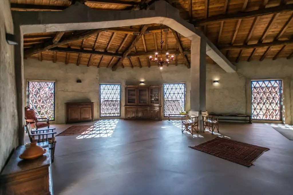 Dopo l'intervento: grande sala sotto il tetto in legno a vista, telaio rinforzato e intonacato, finestre con grate a losanga e luce che filtra sul pavimento